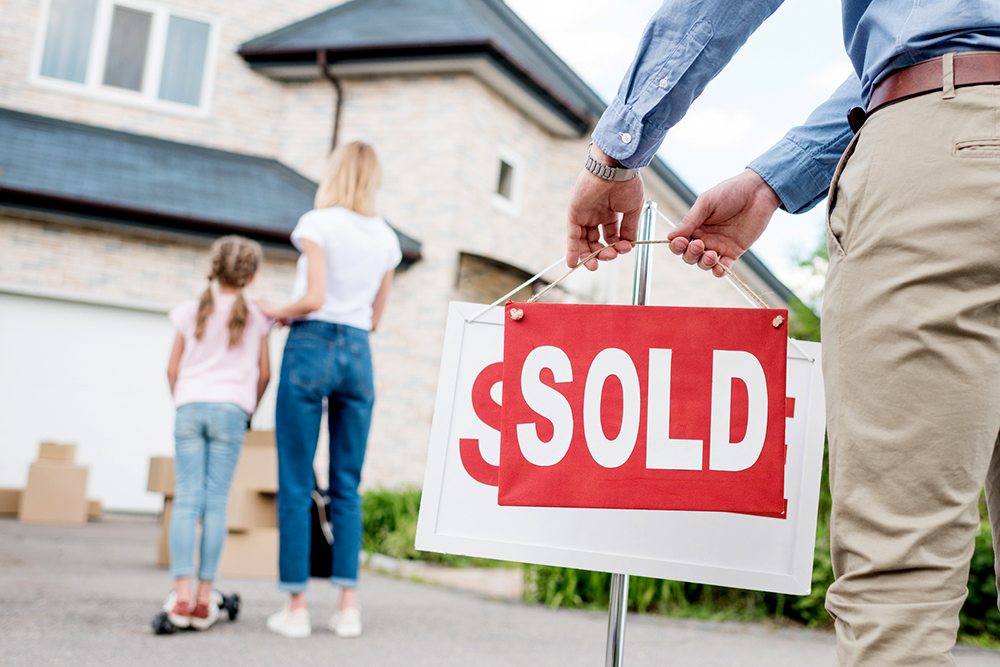 realtor putting a sold sign in front of a a house bought by a mom after a thorough home inspection